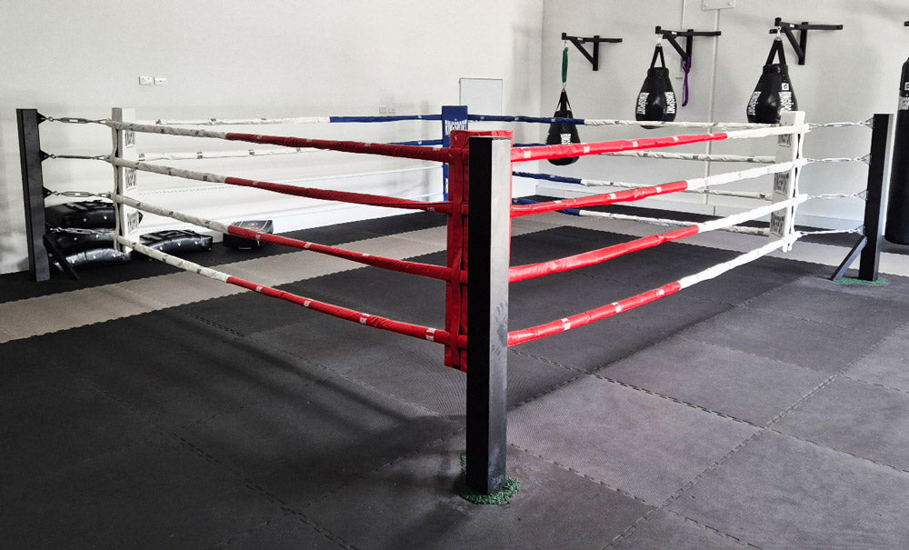 Boxing floor ring with red and white ropes in a Muay Thai gym setting