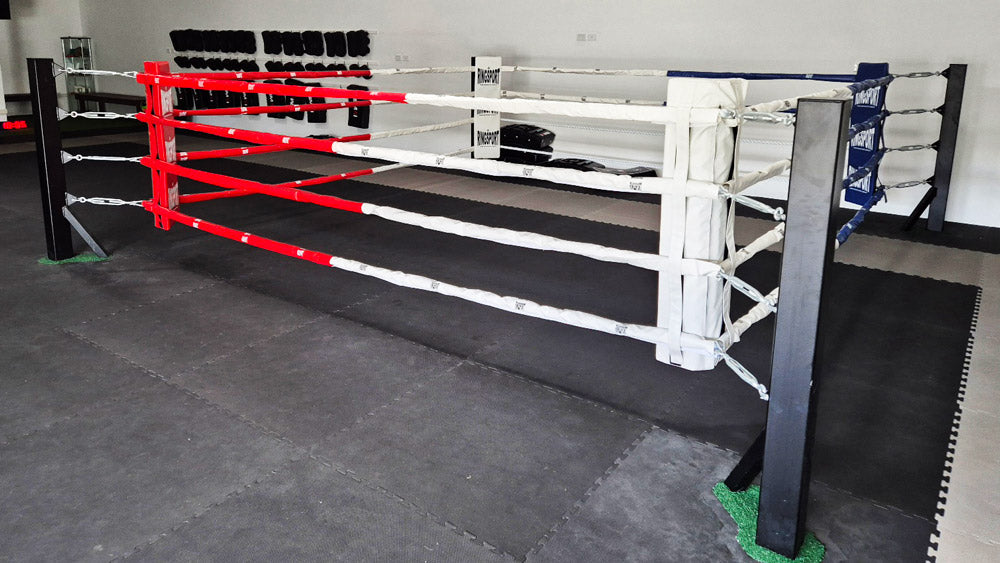 Boxing ring with red and white ropes and black corner posts in a boxing gym 